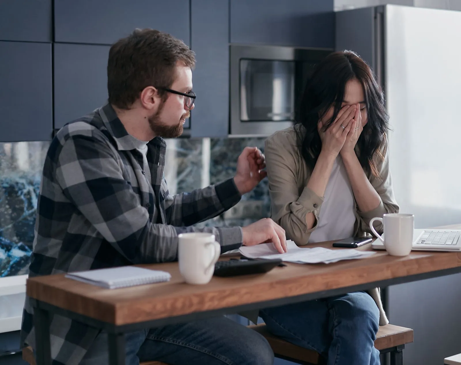 A couple reviews bills and a laptop at their kitchen table.